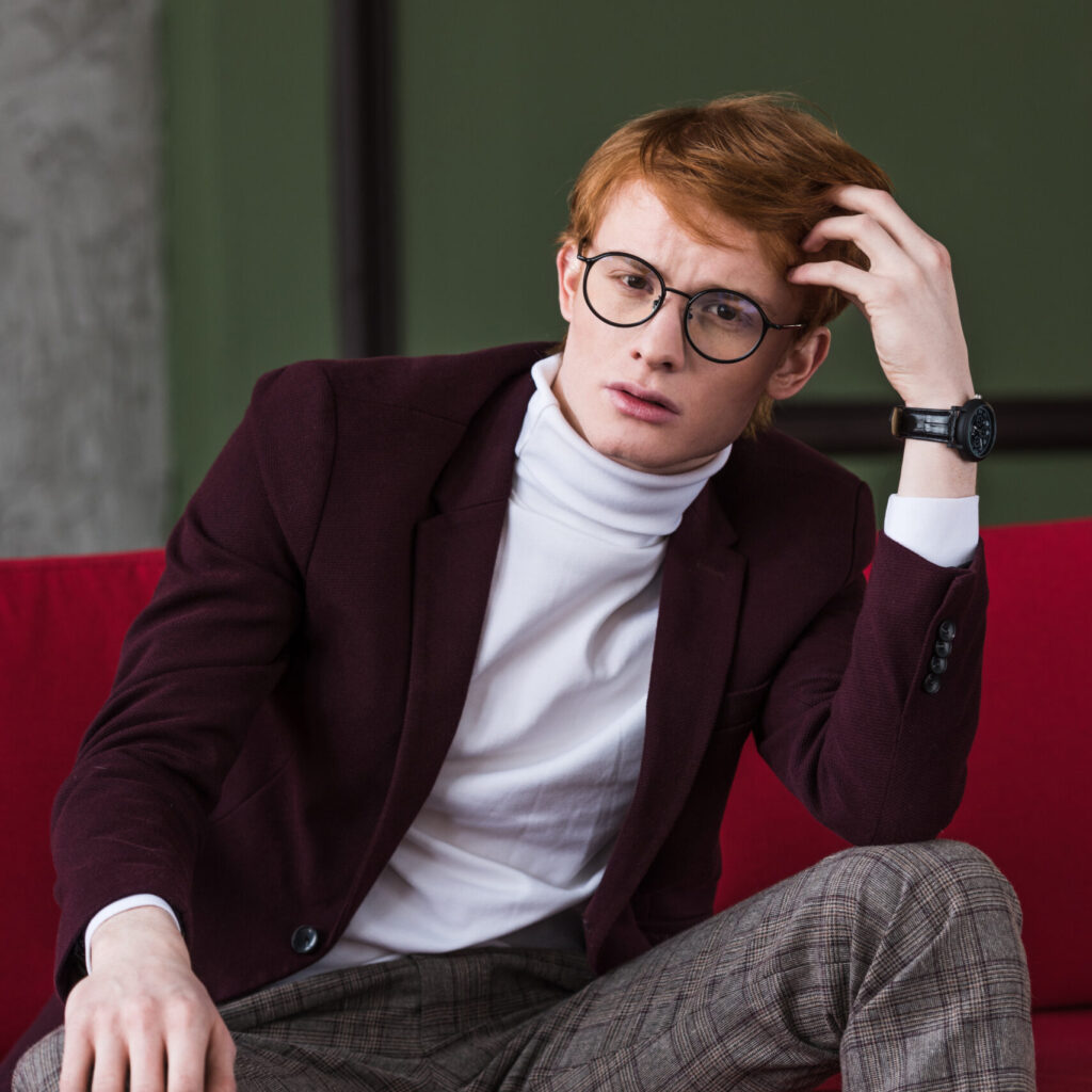 portrait of young male fashion model in eyeglasses sitting on couch